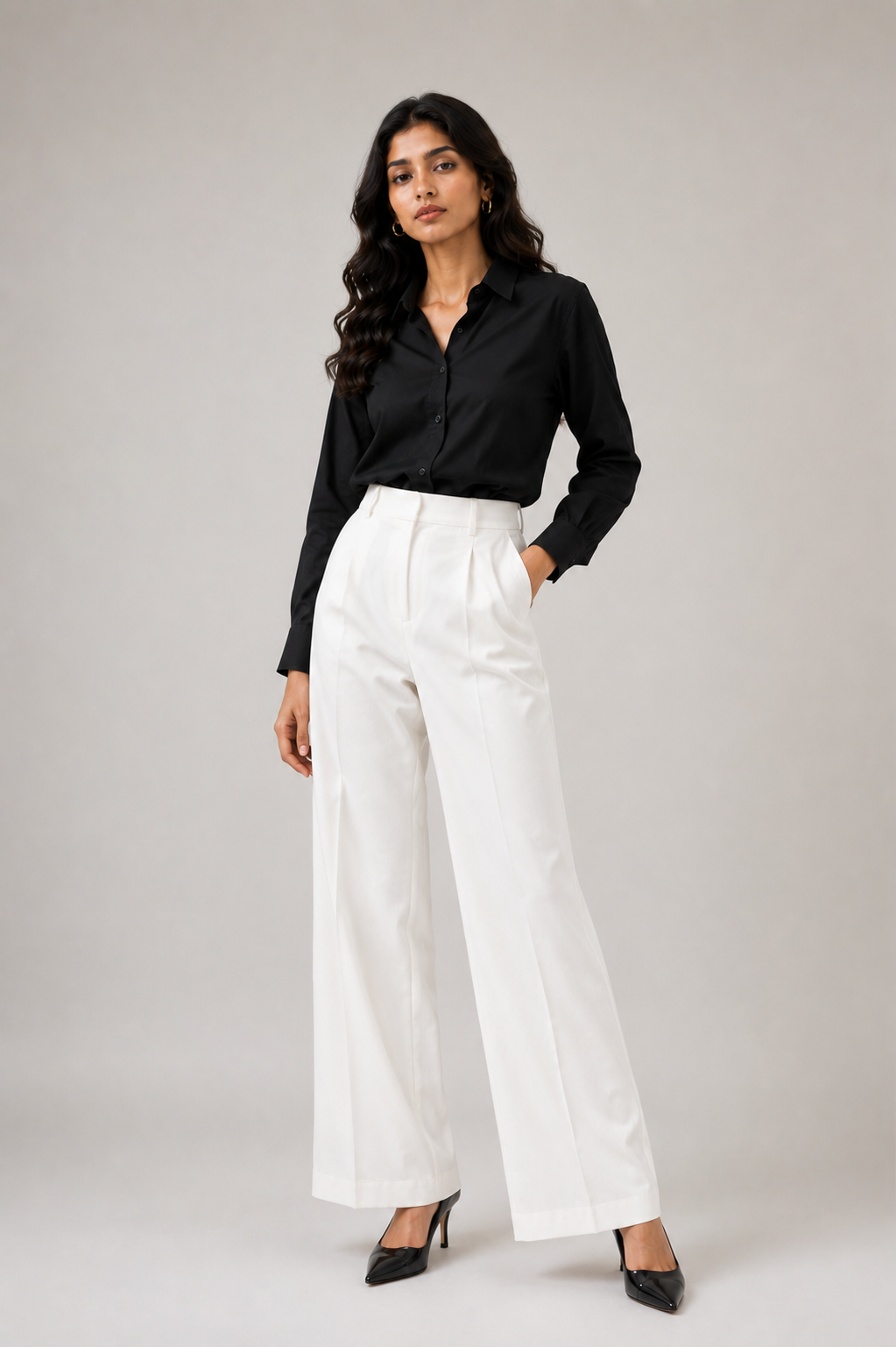 A woman modeling a white long-sleeve button-up shirt tucked into black high-waisted trousers, photographed against a clean light gray studio background.
